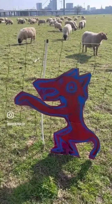 Painted wolf figure on a board in a field among sheep, Art Is Trash